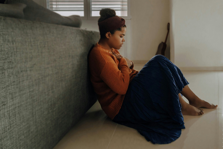 girl sitting on the floor against a couch holding her chest looking anxious