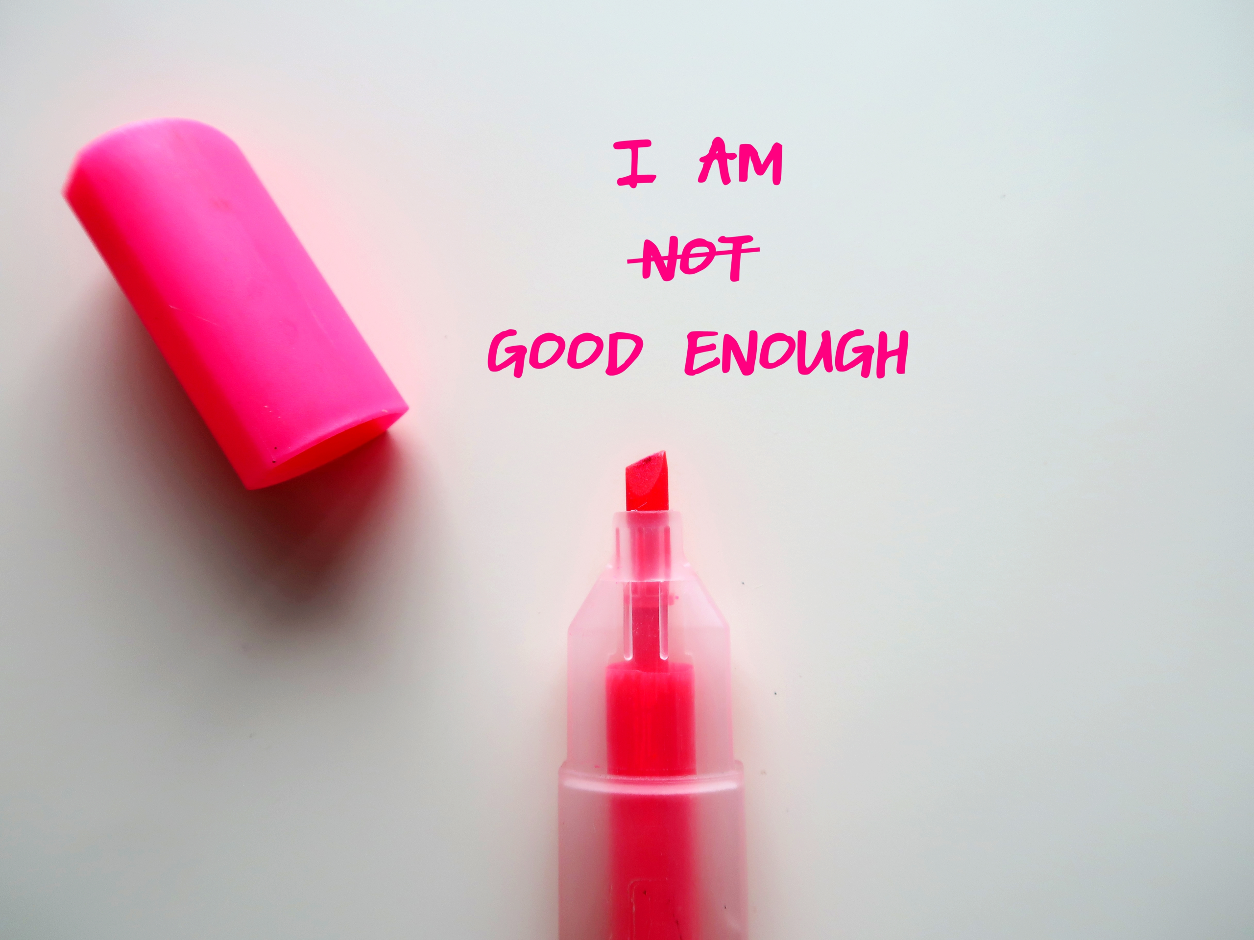 A pink marker with its cap off lies next to the words I am not good enough, with not crossed out to read I am good enough—a bold reminder to break free and boost your self-worth.